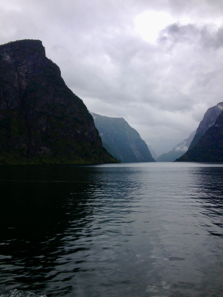 Muted monochrome-style photo of Norway's Sognefjord with steep dark cliffs and misty water.