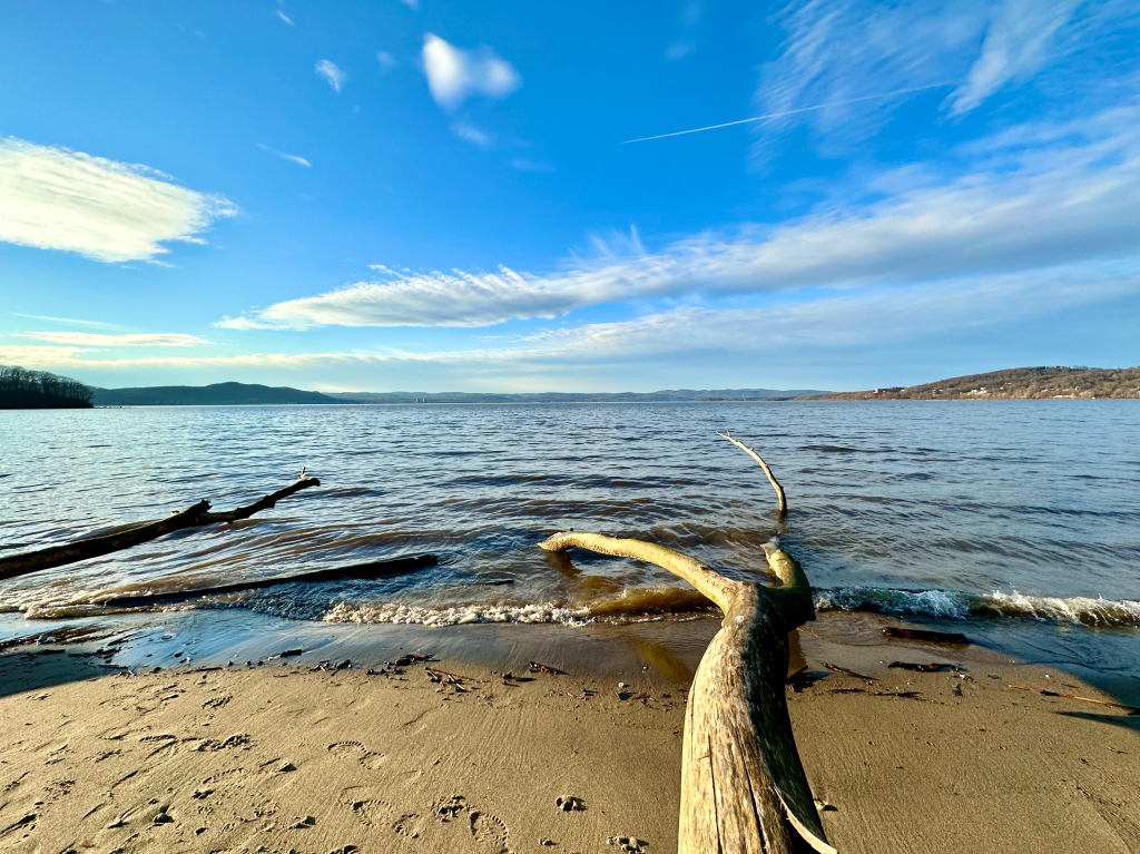 Choppy waves crashing on Hudson River shoreline with blue sky above.