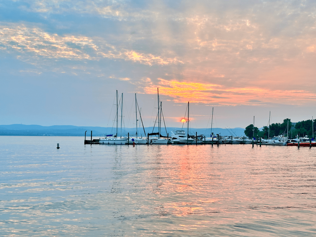 Soft pink and orange sunset over a marina with sailboats lined up on calm water.