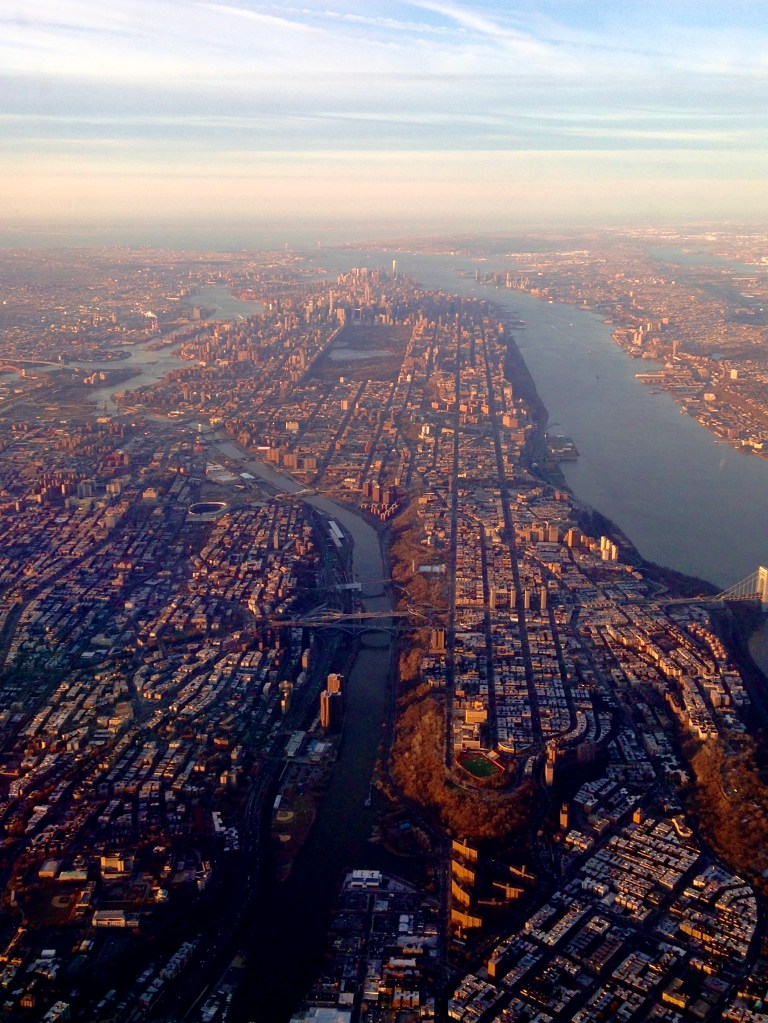 Aerial view of a city skyline with a river and bridges, showcasing urban architecture and waterways during sunset.
