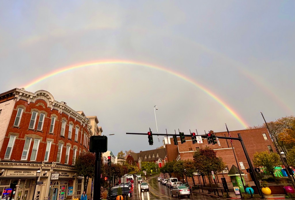A colorful double rainbow after the rain, arching over a suburban downtown area.