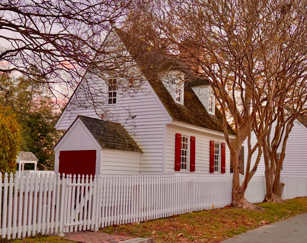 A small white cottage with red shutters in the colonial style architecture at Colonial Williamsburg, Virginia.
